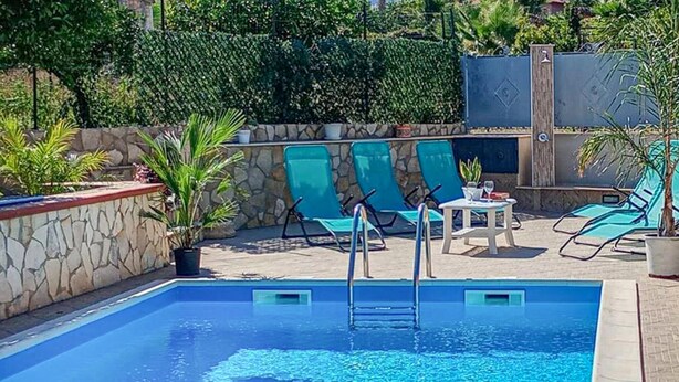 A swimming pool with clear blue water, surrounded by stone walls and green chairs.