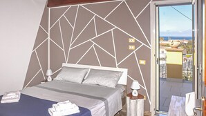 A bedroom with a geometric-patterned wall, a bed with pillows, a nightstand with a lamp, and a view of the outside through a glass door.