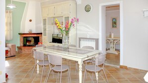 A dining area with a table, chairs, a fireplace, and a kitchen in the background.