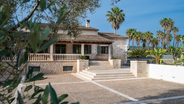 A Mediterranean-style villa with a stone facade, a tiled roof, and a stone staircase leading to the entrance.