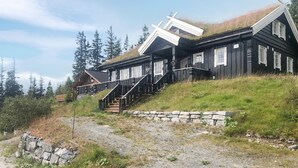 A cabin with a stone retaining wall, wooden stairs, and a grassy hillside.