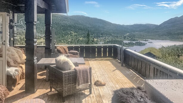 A wooden deck with wicker furniture and a view of a lake and mountains.