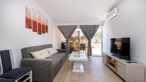 Una sala moderna con un sofá gris, una mesa de centro, un televisor y un balcón con vistas.