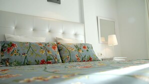 Una habitación de hotel con cabecera capitonada, ropa de cama con estampado floral, una lámpara de noche y un espejo en la pared.