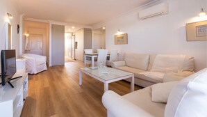 Una sala moderna con un sofá, una mesa de centro de vidrio y un televisor. Hay un comedor con sillas y una mesa.