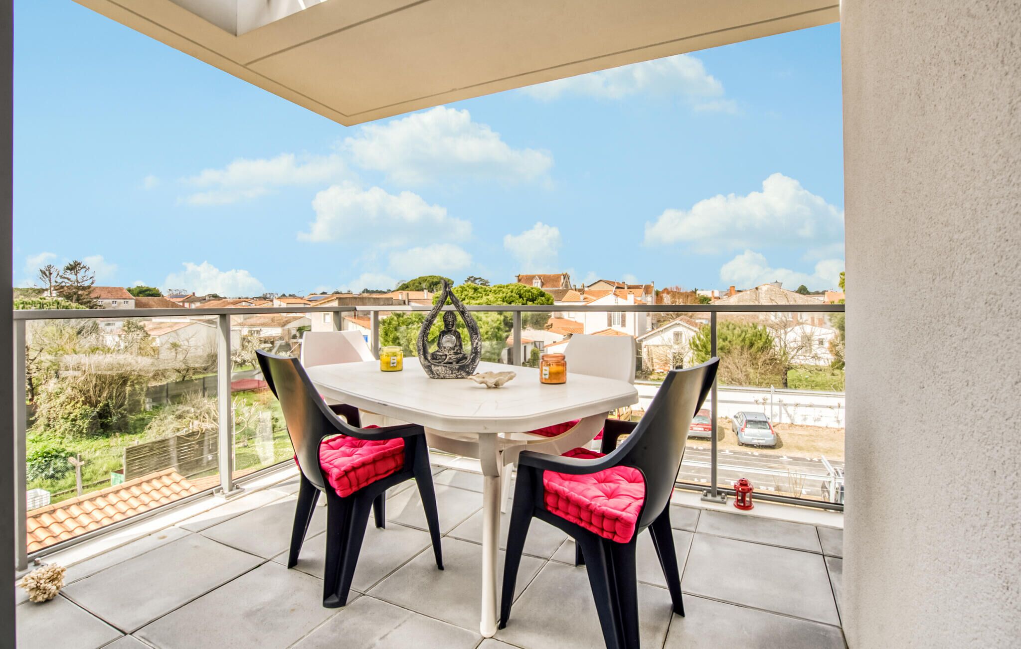Un balcón con una mesa y sillas, una estatua de Buda y vistas a casas y follaje.