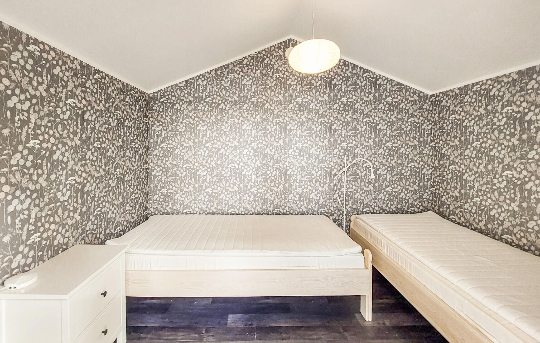 Una habitación con dos camas, un tocador blanco y una pared con estampado floral.