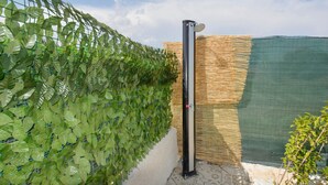 En lodret havevæg med grøn vegetation mod en netlignende baggrund, en sort stang med en rød knap og et afspærret område med net.
