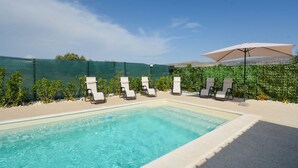 En swimmingpool med liggestole og et hegn i grøn farve i baggrunden.