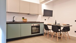 A modern kitchen with a built-in oven, a dining area with a table and chairs, and a flat-screen TV mounted on the wall. - Stunning apartment in Trappeto with WiFi (Trappeto)