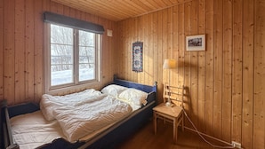 Una camera in una baita di legno con un letto, un tavolino, una lampada e una finestra vista su un paesaggio innevato.