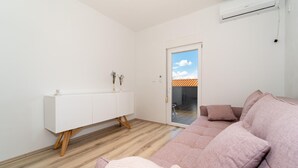 Ett modernt vardagsrum med ett vitt skåp, en rosa soffa och en skjutdörr i glas som leder ut till ett utomhusområde med ett tak täckt av kakel.