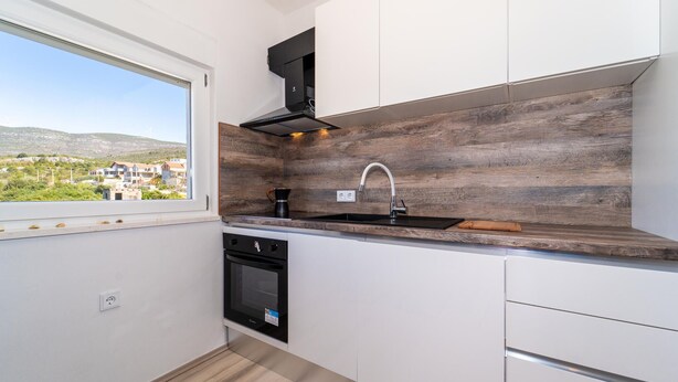 Ett kompakt kök med en inbyggd ugn, en diskho och ett fönster med utsikt över ett bostadsområde.