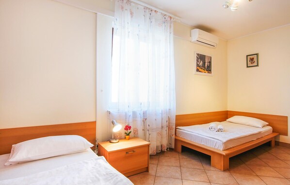 A hotel room with two beds, a nightstand with a lamp, a potted plant, and a window with floral curtains.