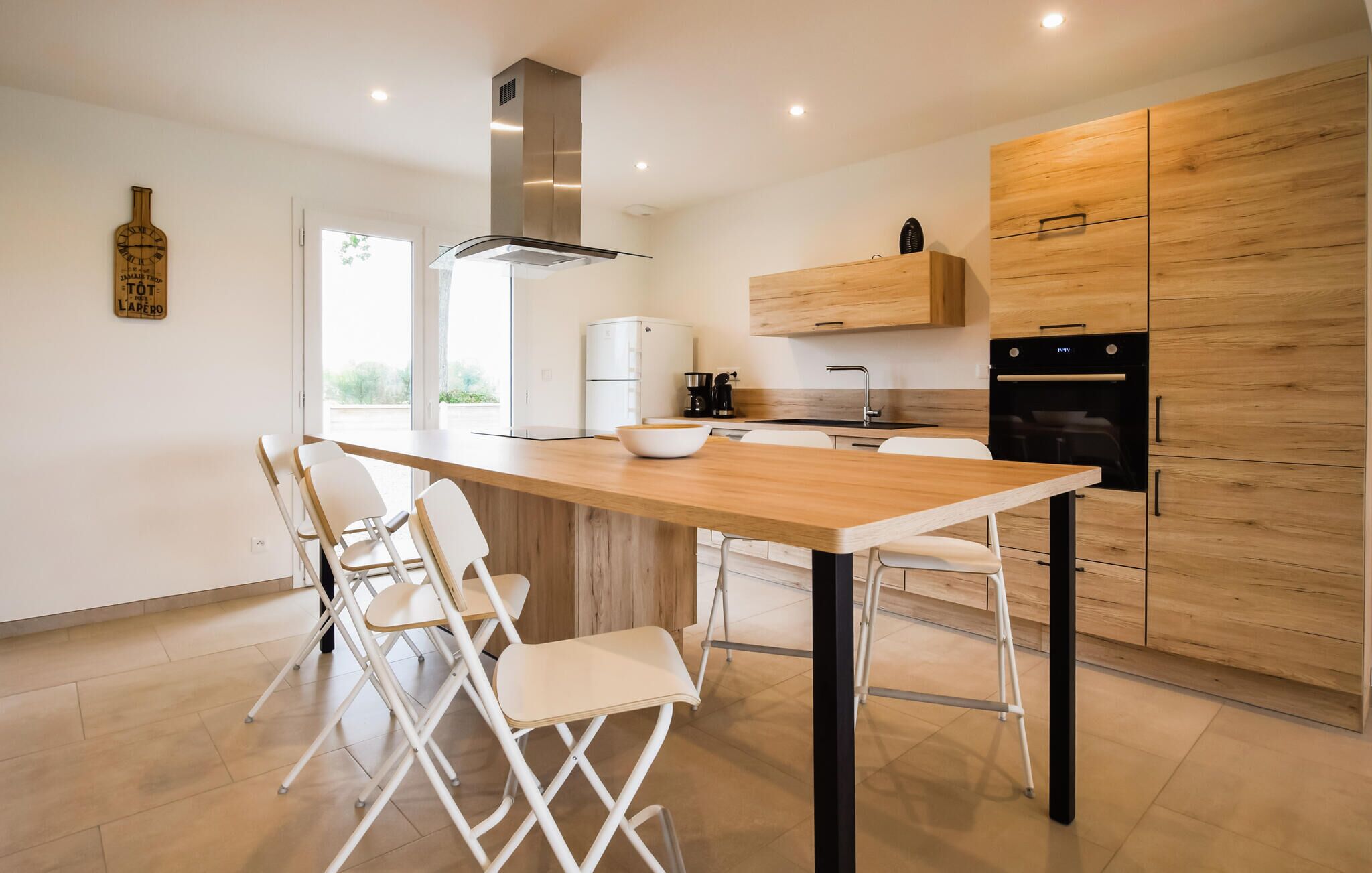 A modern kitchen with a wooden table, white chairs, a built-in oven, and a stainless steel range hood.