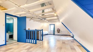 A room with a sloped ceiling, wooden flooring, a bed, a desk, and a window.