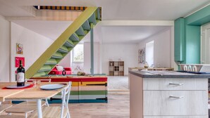 A modern kitchen with a wooden dining table, chairs, a colorful bench, and a green staircase.