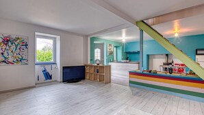 A spacious living room with a large TV, wooden shelves, and a colorful play area.