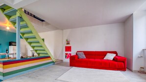 A modern living room with a vibrant staircase, a red sofa, and a white rug.