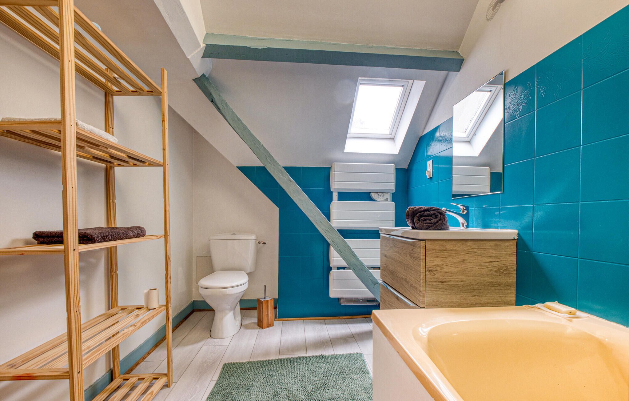 Een badkamer met een houten plank, toilet, badkuip en dakraam.