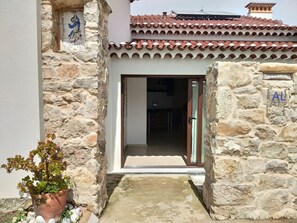 A stone building with a tiled roof, a potted plant, and a door leading to an interior space.