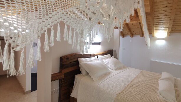 Een slaapkamer met een houten hoofdbord, wit beddengoed en een hangende macramé decoratie.