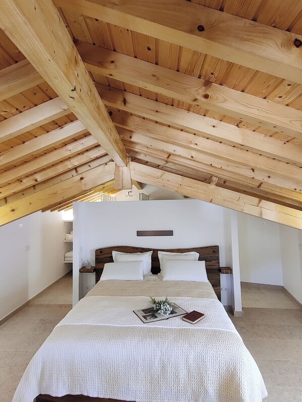 A bedroom with a wooden ceiling, a bed with white bedding, a nightstand, and a wall-mounted light fixture.