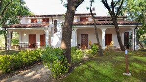 A two-story building with a tiled roof, white walls, and wooden doors. There are two balconies with railings, and a paved pathway leading to the entrance.