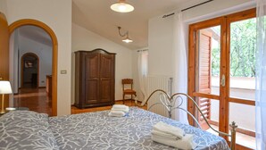 A bedroom with a bed, a wardrobe, a chair, and a balcony with a wooden door.