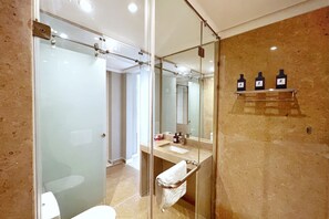 A modern bathroom with a glass shower enclosure, a sink with a towel rack, and a mirror with a shelf holding three bottles.