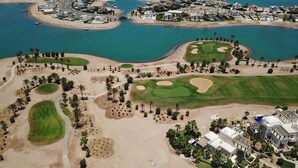 Luchtbeeld van een kustresort met diverse golfbanen, zandstranden en een jachthaven.