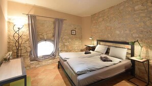 A bedroom with a stone wall, a bed with pillows, a nightstand with a lamp, and a window with curtains. - Beautiful home in Porec (Porec)