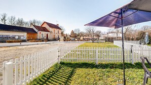 Eine ländliche Straße mit weißem Zaun, einem Gebäude mit dem Schild 'MAIRIE' und einer Flagge.