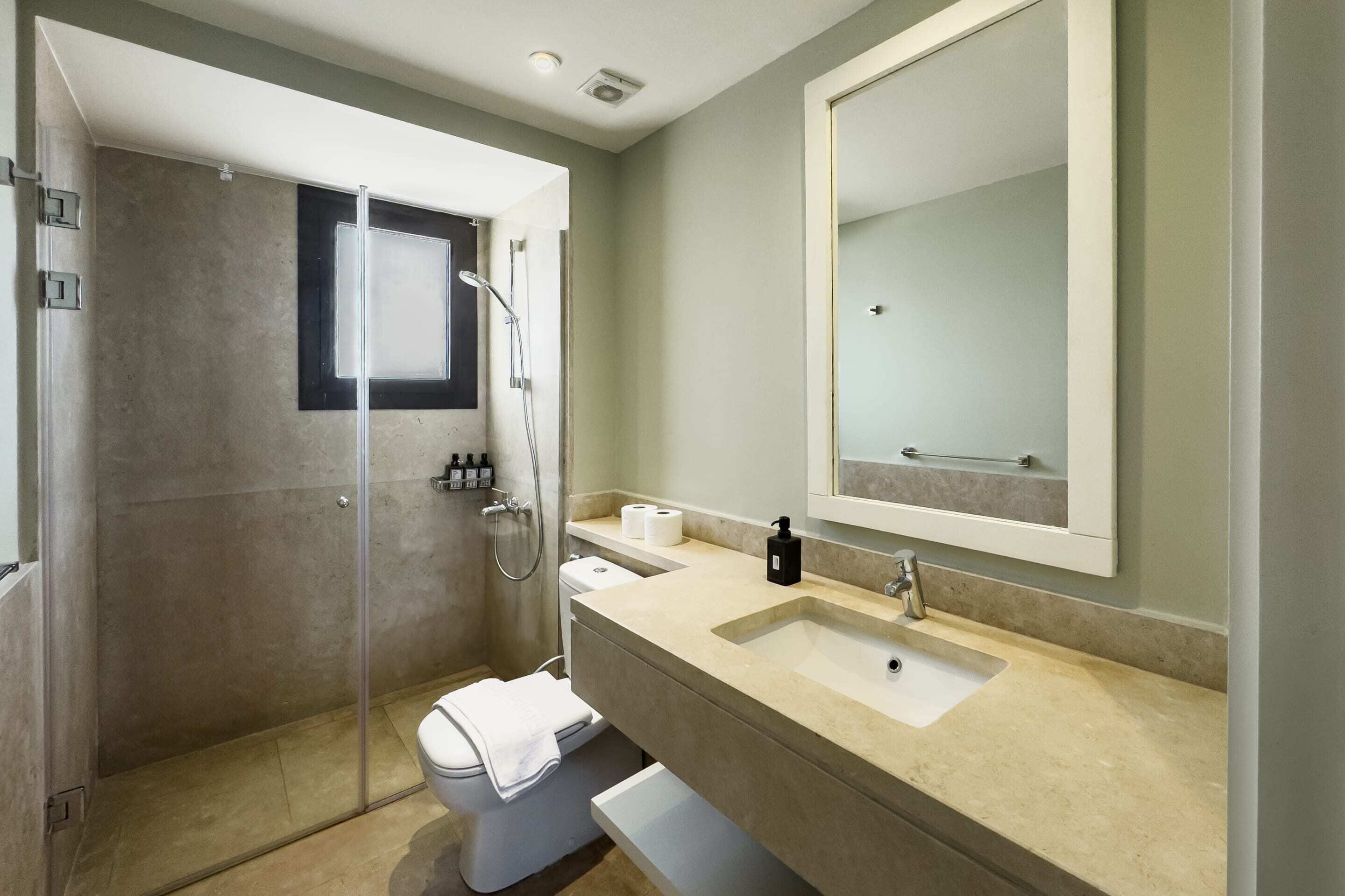 Ein modernes Badezimmer mit einer Glaskabine zur Dusche, einer weißen Toilette und einem beige gefärbten Waschtisch mit großem Spiegel.