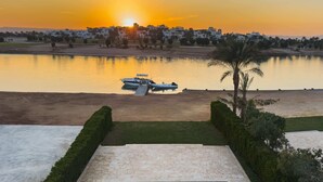 A swimming pool with a view of a sunset over a body of water, a boat, and a row of houses in the background. - Xuru Stays I Sundown Symphony 4mbdr Villa @ Joubal El Gouna (El Gouna)