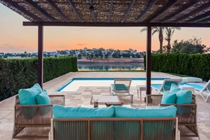 A covered outdoor area with a pool, lounge chairs, and a view of a town in the distance. - Xuru Stays I Sundown Symphony 4mbdr Villa @ Joubal El Gouna (El Gouna)