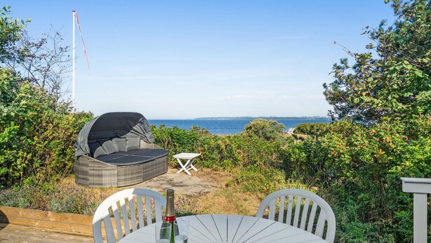 Eine Terrasse mit Sitzgelegenheiten im Freien, Blick auf das Meer und eine hohe Struktur im Hintergrund.