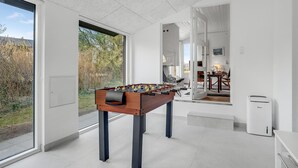 Ein modernes Zimmer mit einem Tischfußballspiel, großen Fenstern und Blick ins Freie.