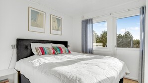 Ein Schlafzimmer mit einem großen Bett, einem Fenster mit Vorhängen und zwei gerahmten Bildern an der Wand.