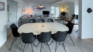 Ein modernes Wohnzimmer mit einem großen, ovalen Esstisch, umgeben von schwarzen Stühlen, einer Couch und einem Fernseher.