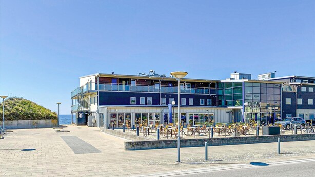 A waterfront hotel with outdoor seating, a view of the sea, and a modern architectural design.