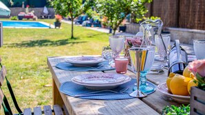 A wooden picnic table set outdoors with plates, cutlery, and a pitcher of water. - LUXURY SINGULAR VILLA ROSA (PADRON)