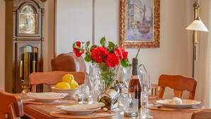 A dining table set with plates, glasses, a vase with red flowers, lemons, and wine bottles. - LUXURY SINGULAR VILLA ROSA (PADRON)