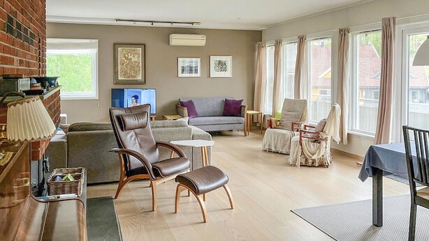 Un salon comprenant un canapé, deux fauteuils, une table basse et un téléviseur. Les fenêtres sont dotées de rideaux, il y a une cheminée et des œuvres d’art ornent les murs.