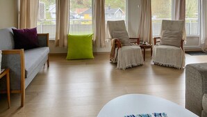 Un salon comprenant un canapé, deux fauteuils, une table basse et un pouf vert vif.