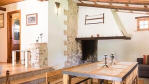 A rustic interior with a stone fireplace, wooden beams, and a dining table with a glass top.