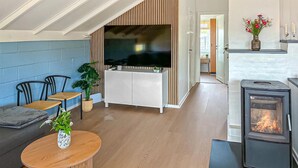 Ein modernes Wohnzimmer mit Fernseher, Sitzgelegenheiten, Kamin und Küchenzeile.