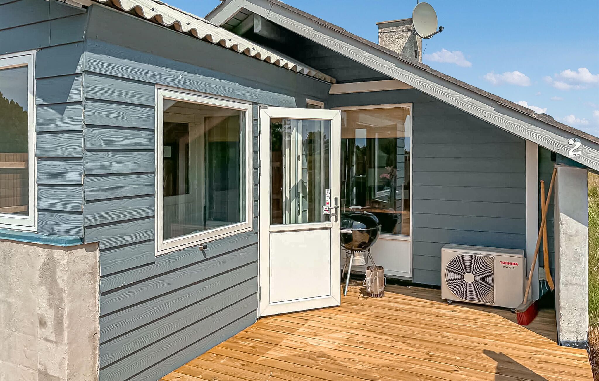 Un bâtiment bleu doté d’une terrasse en bois, d’une porte-fenêtre coulissante et d’une antenne parabolique.