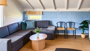 Ein modernes Wohnzimmer mit einem Ecksofa, zwei Sesseln, einem runden Holztisch und einem Blumentopf.