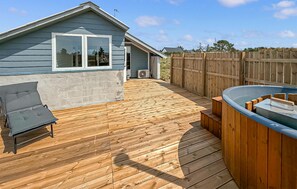 Een houten terras met een bubbelbad, een overdekte patio en een huis met een raam.